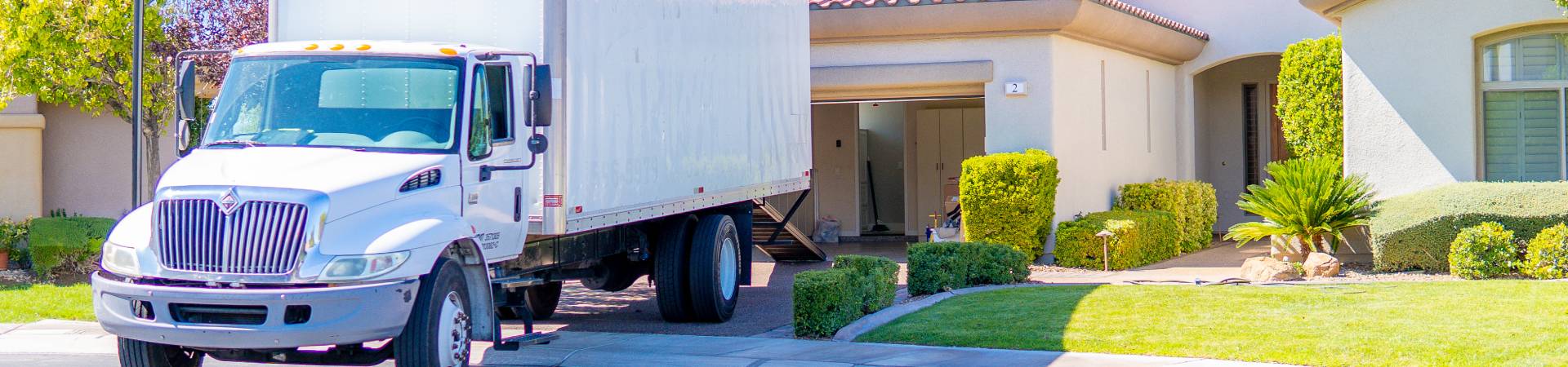 A Muscle Movers box truck parked in front of a home with a tidy front yard.