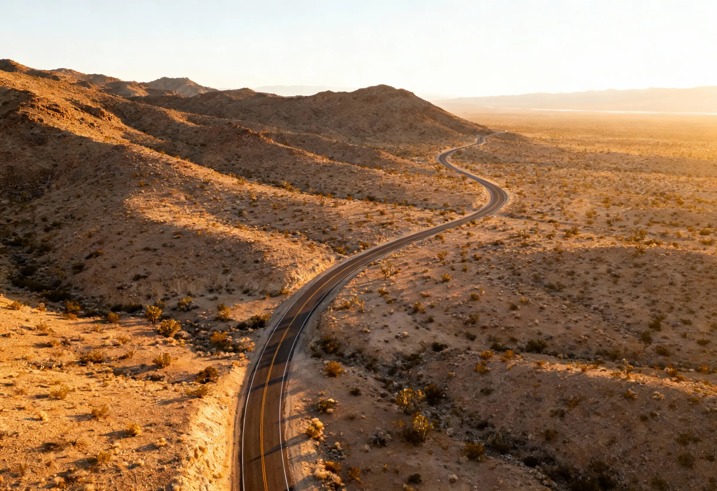 Aerial view of a road winding through desert hills at sunset.