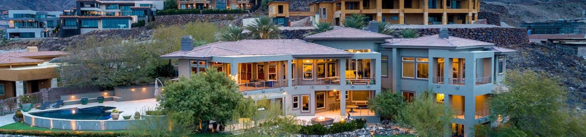 A large hillside home with a pool, lit at dusk.