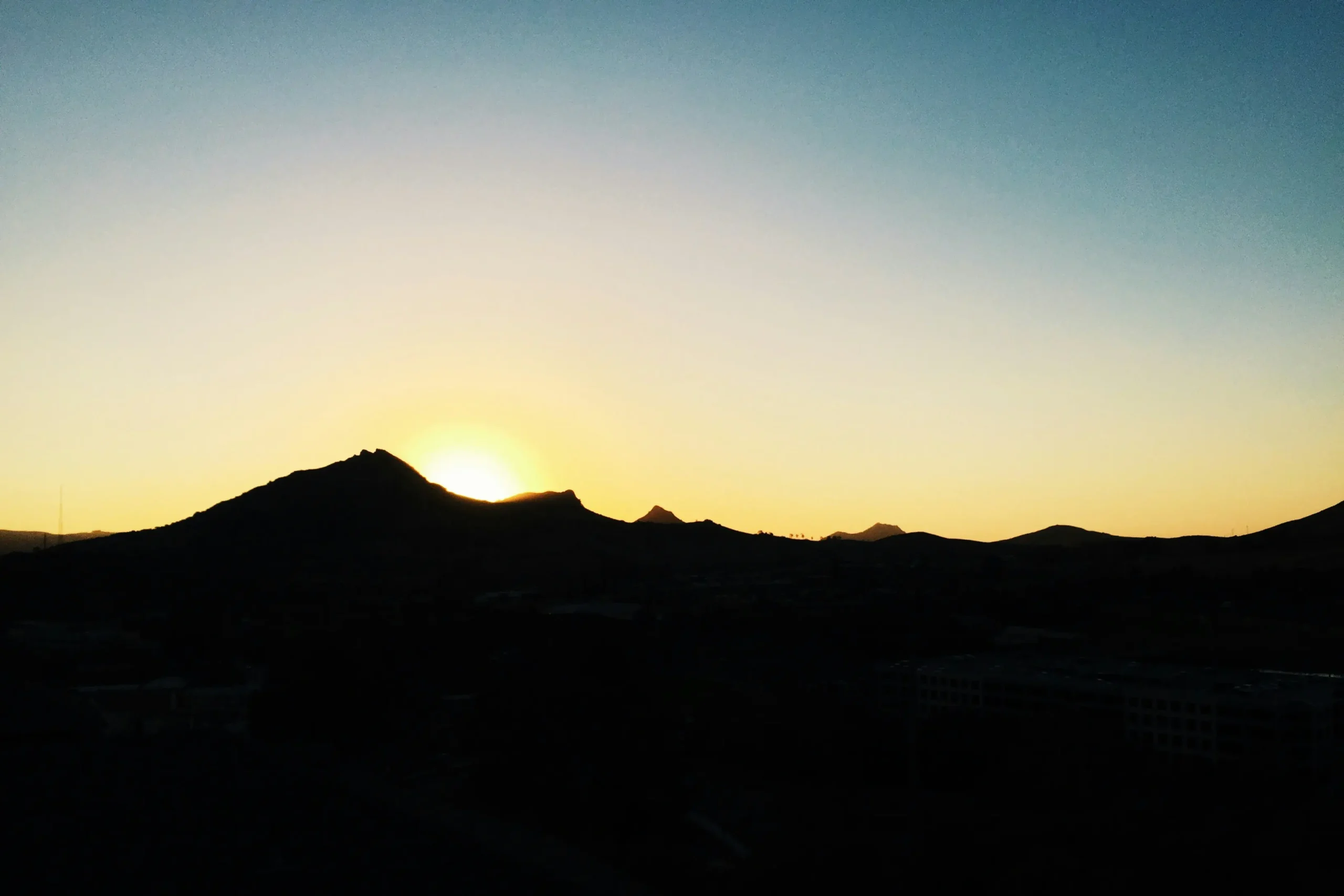 The sun rising behind a desert mountain silhouette.